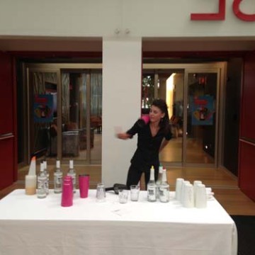 Person behind a table with bottles and cups, in a hallway setting.