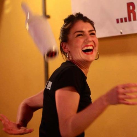 Smiling woman juggling a bottle indoors under warm lighting.