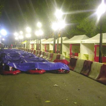 Street with barricades, tents, and covered items at night under bright lights.