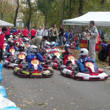 People preparing for a go-kart race on a tree-lined track with tents and onlookers nearby.