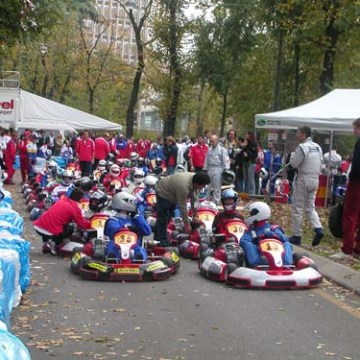 People gather around go-karts lined up on a tree-lined road with tents and spectators.