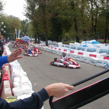 Go-kart race with drivers speeding past on a track lined with barriers and spectators watching.