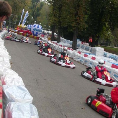 Go-kart race on an outdoor track with drivers in helmets and red suits.