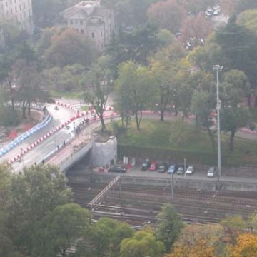 Elevated view of a park with trees, road under construction, and train tracks.