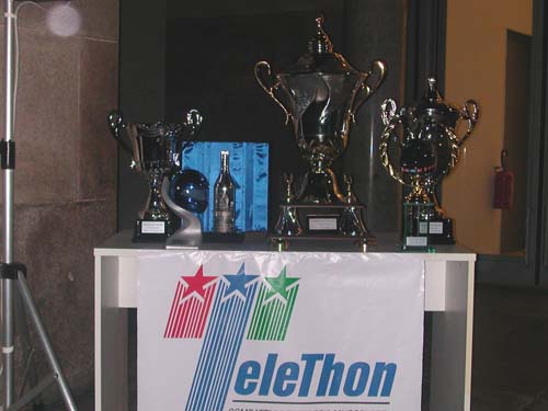 Three trophies on a table with a 'Telethon' banner.