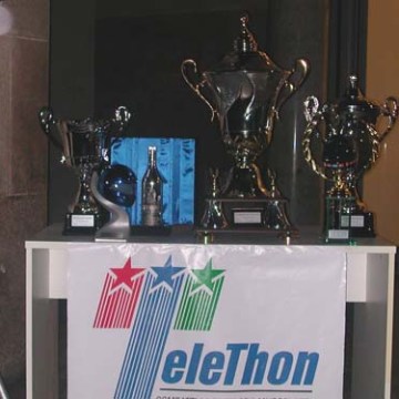 Three trophies on a table with a 'Telethon' banner.