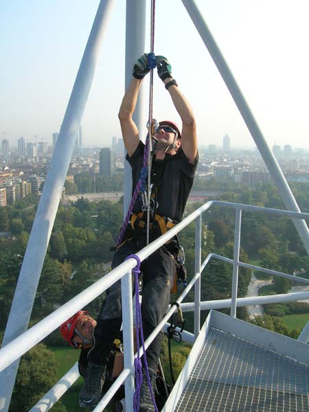 Two people in climbing gear working on a high structure with a cityscape in the background.