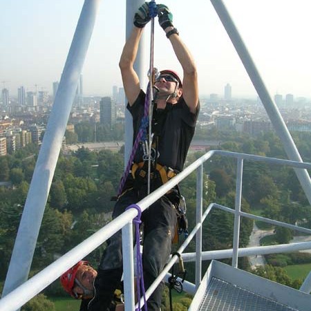 Two people in climbing gear working on a high structure with a cityscape in the background.