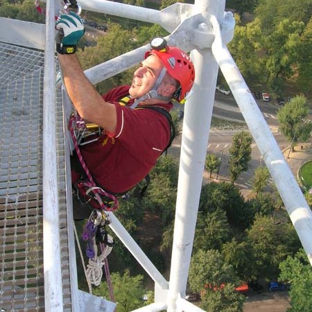 Person in climbing gear ascends a metal structure with trees below.