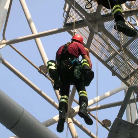Worker in safety gear climbing a metal structure with ropes.