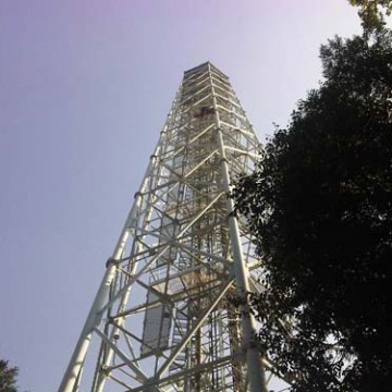 Tall metal tower surrounded by trees against a clear blue sky.