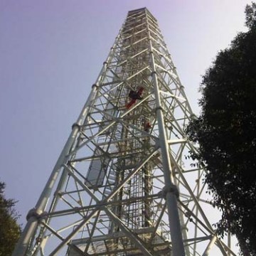 Tall metal tower against blue sky, viewed from below with trees on both sides.