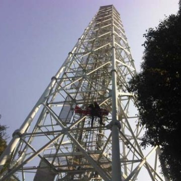 Tall metal tower structure with a person climbing, surrounded by trees under a clear sky.