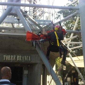 Rescue worker in gear secures person on stretcher at Torre Branca structure.