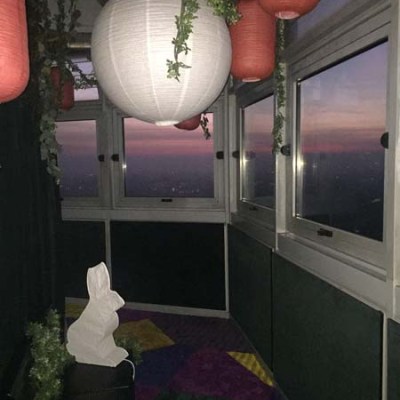 Enclosed balcony with lanterns, plants, and a white sculpture at sunset.