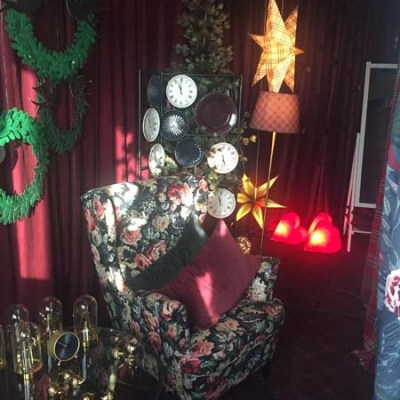 Cozy room with floral chair, star lamps, clock display, and festive wreaths on maroon curtains.