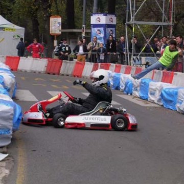 Person in a go-kart wearing a helmet on a track, surrounded by spectators and safety barriers.