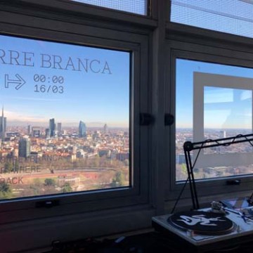 City view through large windows with DJ equipment in the foreground.