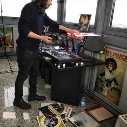 Person in black outfit handling records near a turntable in a room with posters.