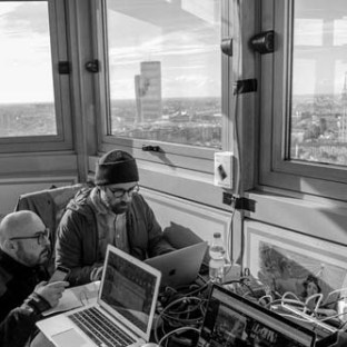 Two people work on laptops in a high-rise room with panoramic city views.