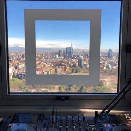DJ equipment in front of a window with a cityscape view containing tall buildings.