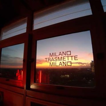 Sunset visible through a window with 'Milano Trasmette Milano' text.