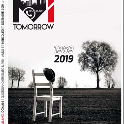 Monochrome landscape with chair, hat, and barren trees. Text: '1969 2019' and 'Mi Tomorrow' logo.