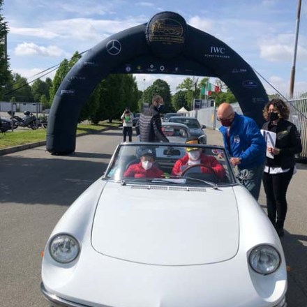 White convertible car with two people, driving under an event archway.