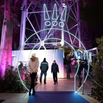 People walking under illuminated arch with exclamation marks above at night.