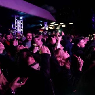 A crowd of people at night, looking up and taking photos with phones.