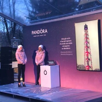 Two people in winter clothes stand near a Pandora display with a lighthouse image.