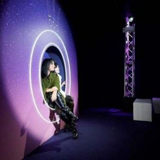 Person sitting in a circular light installation against a starry backdrop.