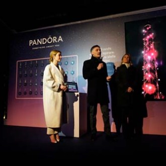 Three people on stage at a Pandora event with a lit display.