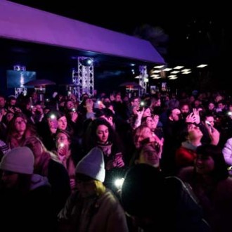 Crowd of people at a night event with stage lights and phones raised.