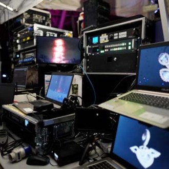 Computers and monitors in a control room with various screens and equipment.