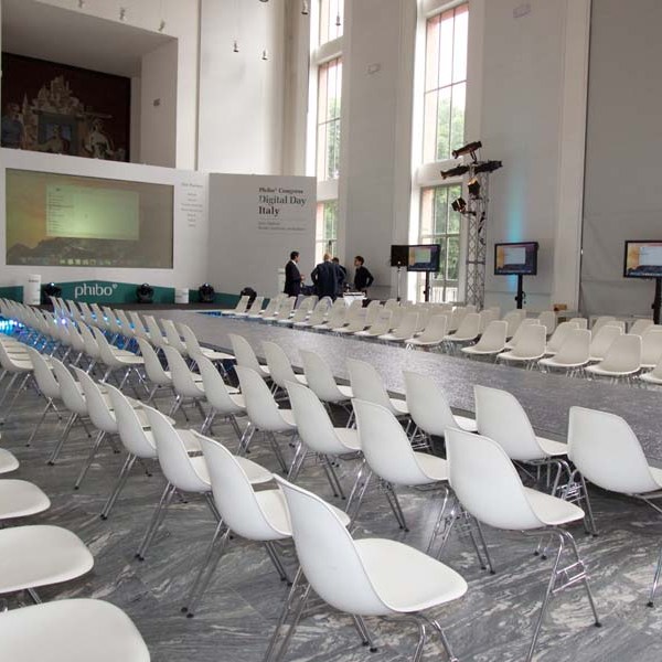Empty conference room with white chairs arranged in rows facing a large screen.
