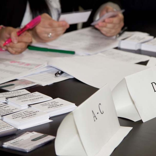 People sorting papers and labels on a table with signs 'A-C' and 'D-I' visible.