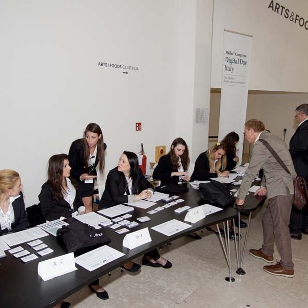People at a registration table with name tags and signs for an event in a room labeled Arts & Foods.
