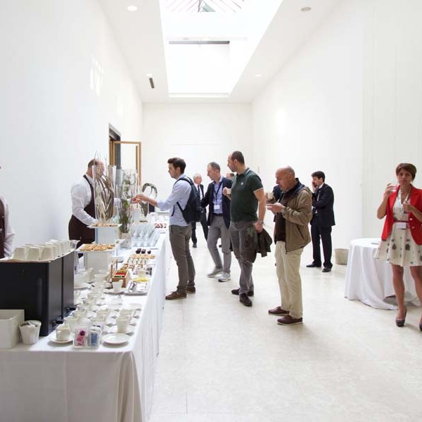 People socializing in a minimalist room with a coffee station on the left.