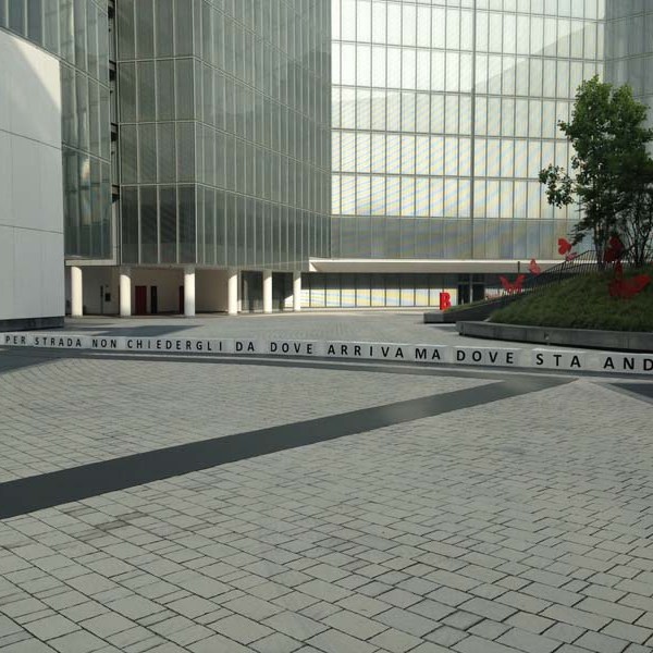 Modern building with 'Vodafone Theatre' sign and paved courtyard, featuring trees and a quote on a low wall.