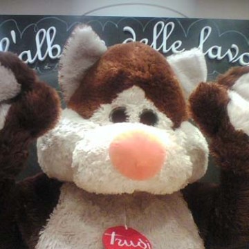 Brown and white plush toy cat with paws raised, standing in front of a blackboard.