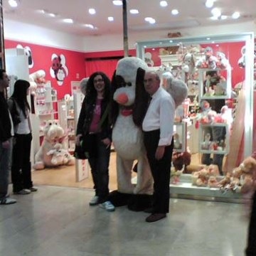 People posing with a large stuffed animal outside a toy store with red walls.