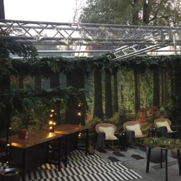 Outdoor seating with forest-themed backdrop, tables, chairs, and string lights.