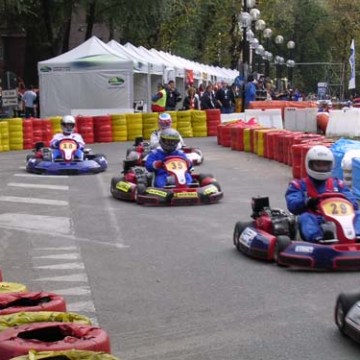 People racing go-karts on a track with colorful tire barriers and tents in the background.