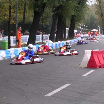 Go-kart race on outdoor track with multiple karts and spectators on the sidelines.