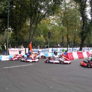 Go-kart race with multiple drivers on a curved track surrounded by trees and spectators.