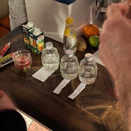 Table with juice cartons, water bottles, lemon, orange, lime, bowl, and a large box.