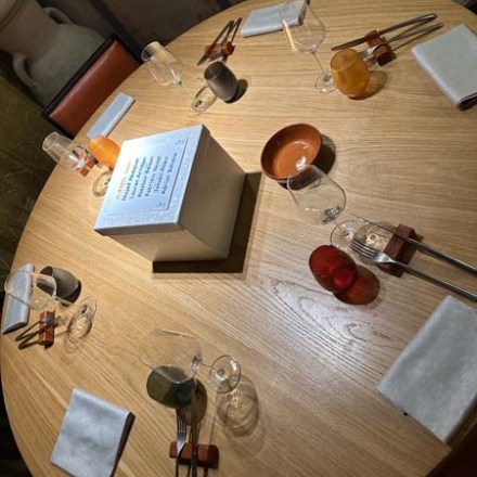 Round wooden table set for six with chopsticks, glasses, napkins, and a white centerpiece.