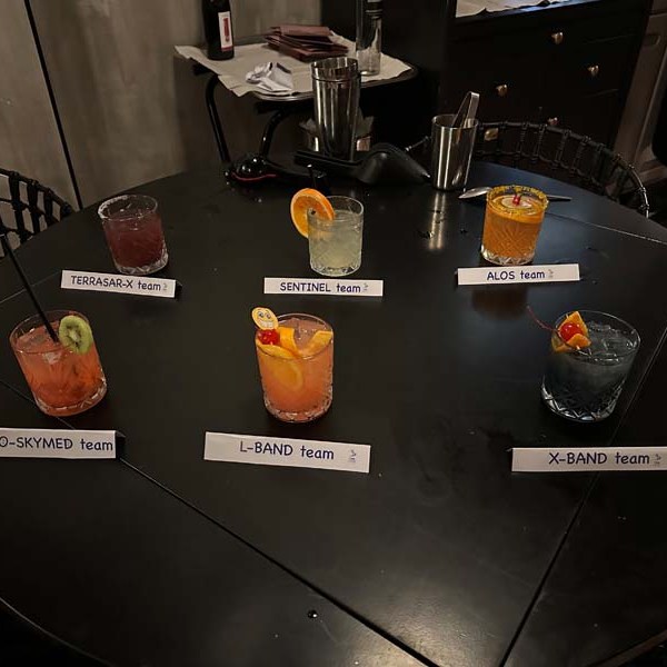 Six drinks with labels on a round table in a dimly lit setting.