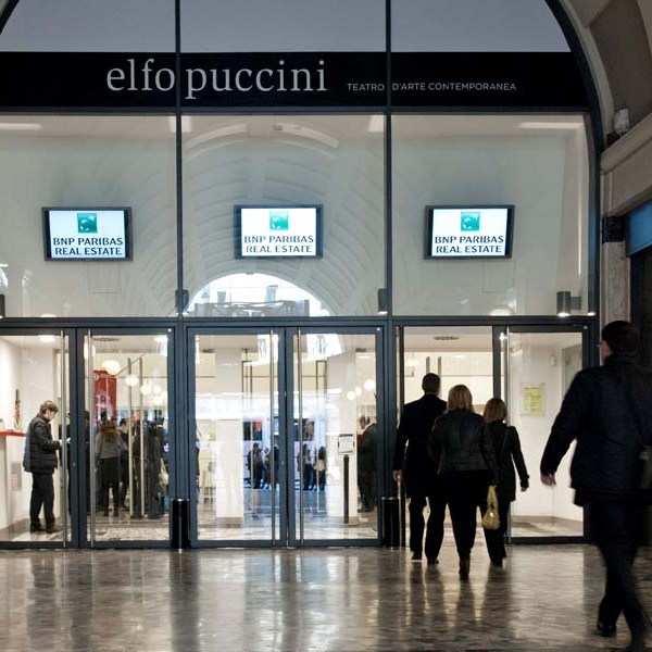People entering Elfo Puccini theatre with BNP Paribas signs above glass doors.